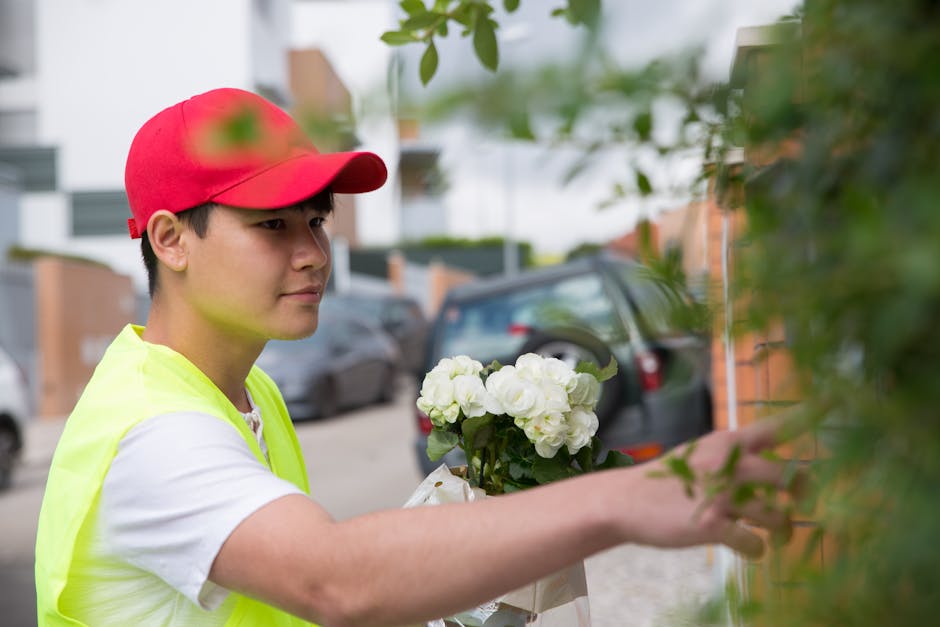 A young delivery person wearing a red cap and a neon yellow vest is seen holding a bouquet of white flowers with green foliage, preparing to deliver it. The bouquet is wrapped in light-colored paper a