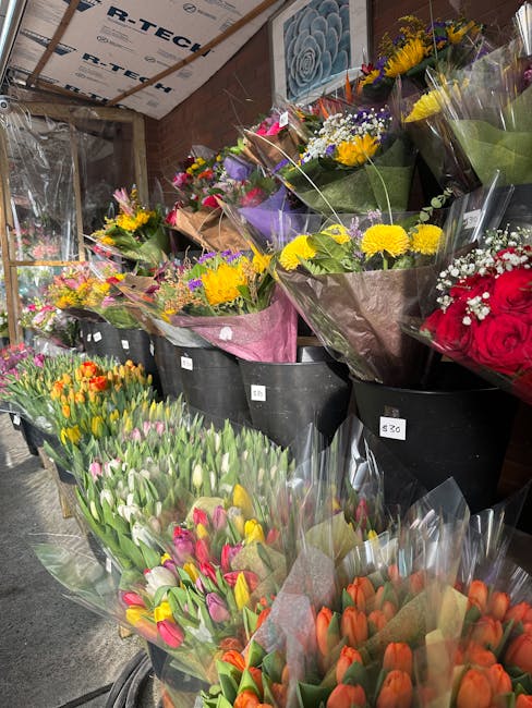 A selection of fresh flower bouquets arranged in black buckets inside a flower shop. The bouquets include yellow chrysanthemums, pink and white tulips, orange tulips, red roses, and mixed arrangements