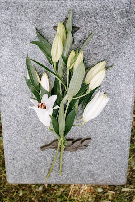 A bouquet of white lilies with green foliage arranged on a gray stone surface. The lilies are in various stages of bloom, with some fully open showing their white petals and deep reddish-brown stamens